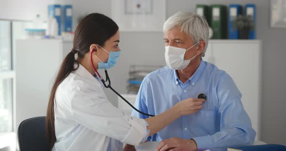 Close Up Serious Doctor Wearing Mask Checking Senior Patient Lungs with Stethoscope