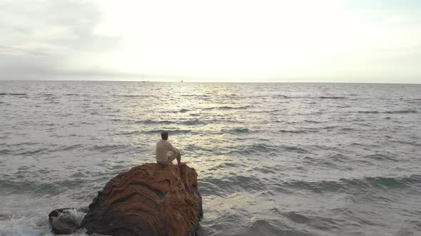 The Guy Sits on a Rock and Looks at the Sunset