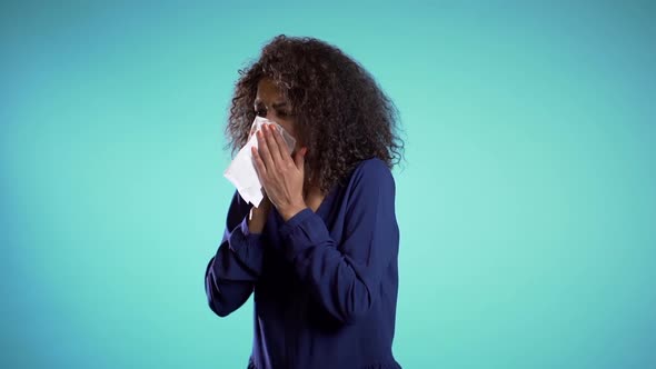 Young girl with afro hair sneezes into tissue. Isolated woman is sick, has a cold