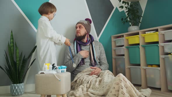 Father and Child Playing Clinic and Doctor Little Boy in Medical Gown with Stethoscope Treats Dad