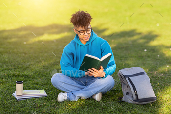 Student reading a book on grass