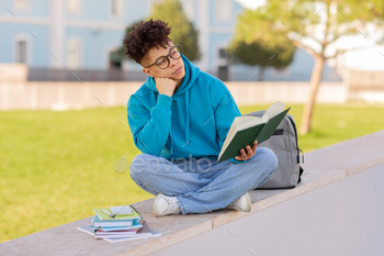 Student with book contemplates on campus