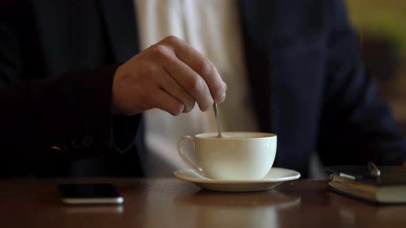 Strong man hands stirring coffee/latte/cappuccino with teaspoon in a cafe. Man dressed in classic bl