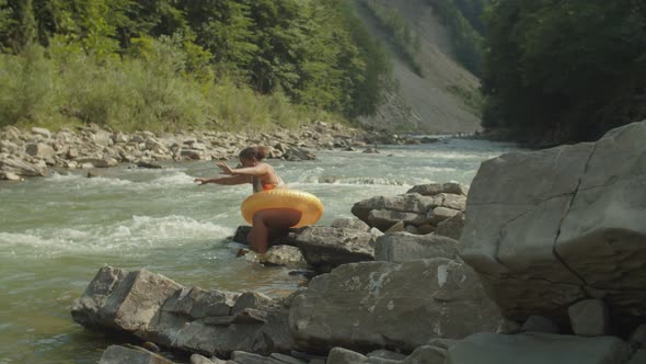 Carefree Pretty Black Female Traveler in Swimsuit and Inflatable Ring Diving Into Rough Mountain