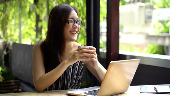 Happy Female Student in Glasses Smiling Using Laptop at Table on Terrace and Studying on Summer Day