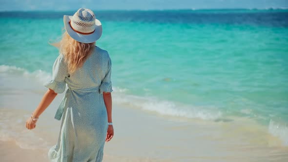 Girl Walking On Ocean Beach.Woman In Hat Walks Along Beach On Caribbean Coast.Dress Blowing In Wind