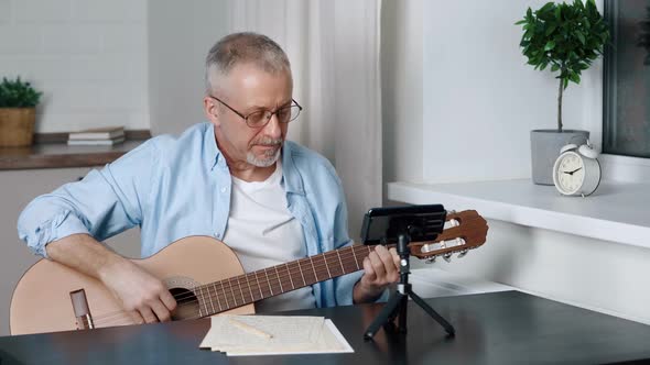 Smiling Middleaged Blogger Plays Guitar While Shooting Video on Smartphone