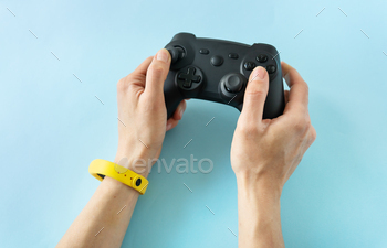 Two hands gripping a black game controller, accentuated by a vivid yellow wristband on a light blue