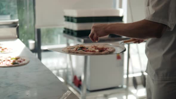 Chef in the Restaurant Prepares a Pizza and Decorates It with Tomato Mozzarella and Basil