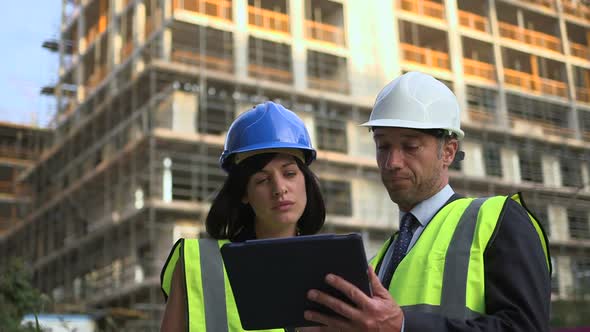 Man and woman discussing with digital tablet at construction site