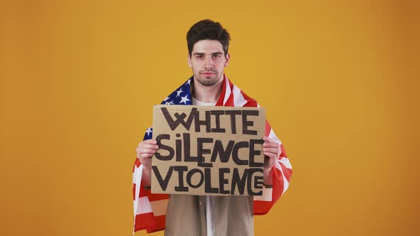 Male Wrapped in Flag of USA is Raising Up Cardboard Poster with Inscription White Silence Violence