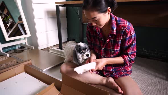 Ethnic woman assembling furniture in room with dog