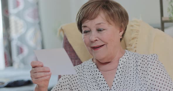 Close Up View of Happy Old Lady Looking at Photo While Sitting on Chair, Emotional Beautiful Woman