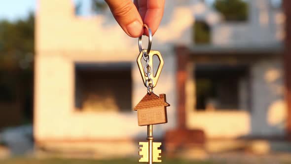 Hand with the key to the future house on the background of a construction site and walls