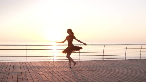 Ballerina in Black Ballet Tutu and Point on Embankment Above Ocean or Sea at Sunrise