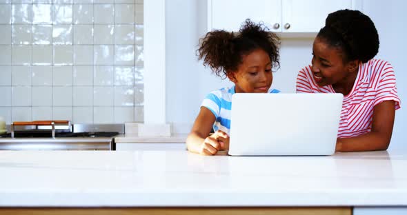 Mother and daughter using laptop in kitchen