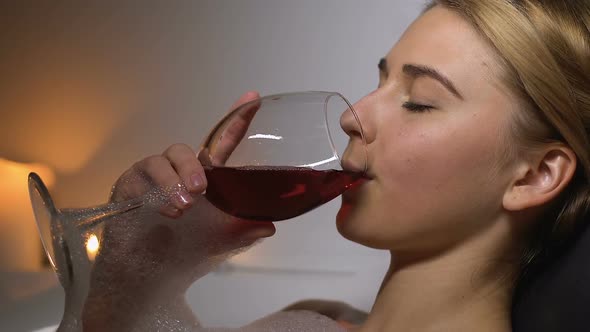 Relaxed Woman Lying in Bath With Aroma Candles, Enjoying Taste of Red Wine, Rest