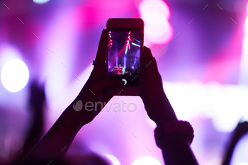 Hand with a phone records live music festival. People taking photographs with smart phone concert.