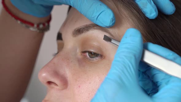 Gloved Hands Pluck Hairs From Eyebrows with Tweezers Closeup