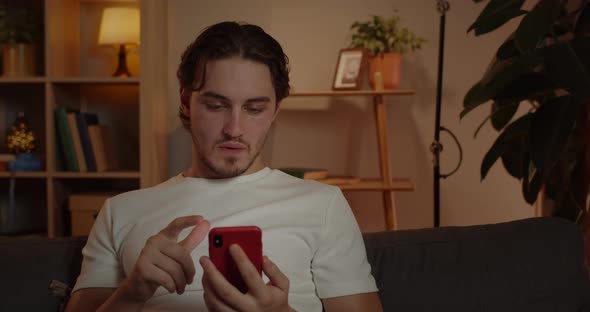 Close Up of Amazed Young Man Scrolling Phone Screen and Saying Wow While Sitting on Couch at Home