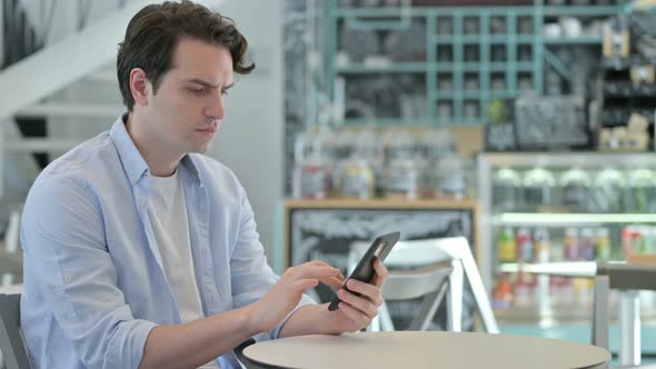 Attractive Young Man Using Smartphone in Cafe