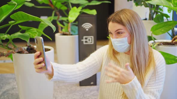 a Young Woman in a Protective Mask Closeup Talking on a Video Call on a Smartphone Next to the Wifi