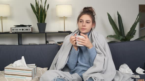 Closeup of a Sick Young Woman Sitting on Sofa with Cup of Tea and Laptop