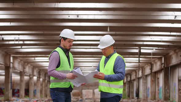 Two Engineers Talk as they Check Information about a Plan in a Hall.