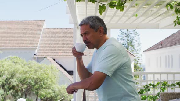 Senior mixed race man drinking coffee on balcony in garden