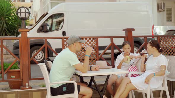 A Family of Three Mom Dad and Daughter are Drinking Lemonade at a Table in a Roadside Cafe in the