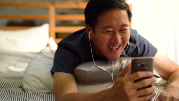 Asian Man Making Facetime Video Calling with Smartphone at Home Waving at People on Phone Screen