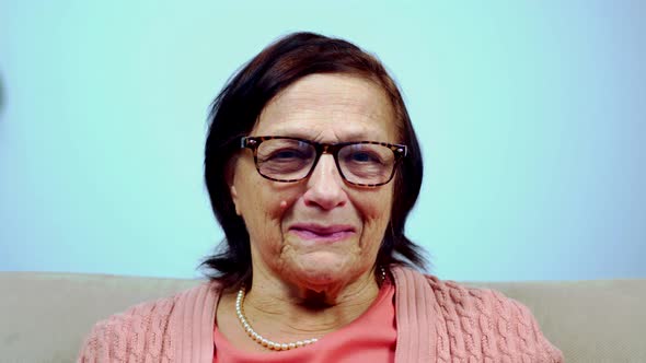 Mature Senior Cheerful Aged Retired Grandmother Sitting On Sofa Looking At Camera. Smiling Portrait