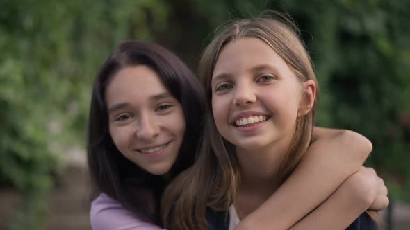 Positive Teenage Girls Hugging Smiling Looking at Camera Standing in Spring Summer Park