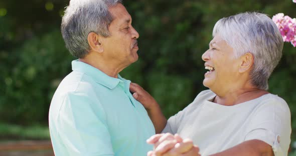 Video of happy biracial senior couple holding hands and dancing in garden