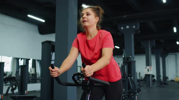 Athletic Young Woman Riding on Spinning Stationary Bike Training Routine in Gym Weight Loss Indoors