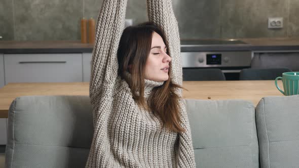 Medium Shot of Young Woman Stretching His Arms and Yawn Sitting in Couch in the Kitchen