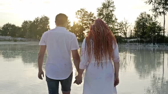 Couple of Lovers at Sunset Go Into the Water of the Lake Holding Hands. Romantic Date.