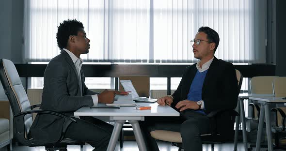 Two Young Businessman Talking at Desk in Office