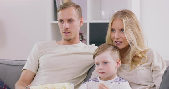 Smiling Young Family with Preschooler Son Sit Relax on Sofa Watching Movie on Tv Eating Popcorn