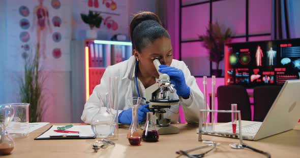 Woman Chemist Learning Biological Samples Under Microscope and Writring Results Into Paper Report