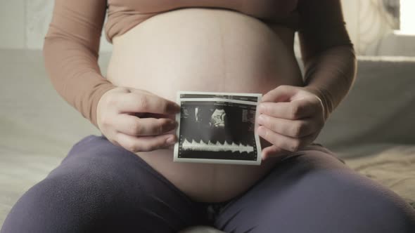 Pregnant Tummy and Female Hands Holding Sonogram Image of Healthy Unborn Baby