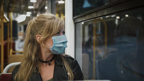 Female Hipster in Protective Mask is Sitting in Moving Tram and Looking Out the Window