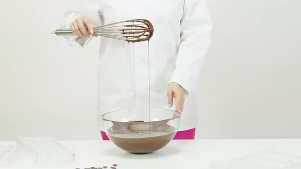 Mixing Smooth Delicious Melted Dark Chocolate with Whisk in Glass Bowl. Closeup
