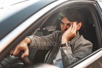 Annoyed tired young man driving his car with open window