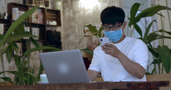 Man with Glasses. Asian-looking Teenager in Protective Mask, Student Working on Phone From Cafe and