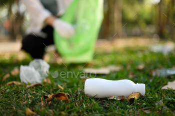 Plastic bottles littering on grass with blurred collecting garbage at the public park.