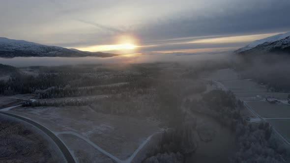 Flying over foggy icy treetops and frozen fields at sunset in Northern Scandinavia Helgeland, Northe