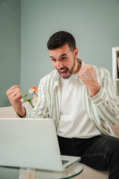 Vertical. Handsome and joyful guy winning a sports bet and celebrating in front of the laptop