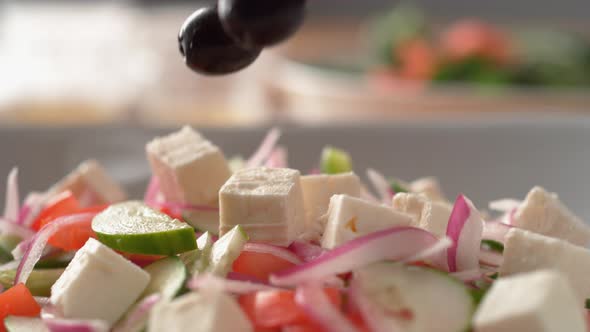 Camera follows putting fresh olive over greek salad. Slow Motion.