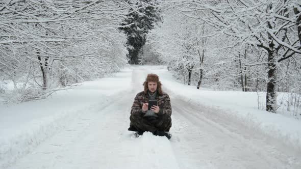 Guy Hiker Sits on the Road in Winter with a Tablet